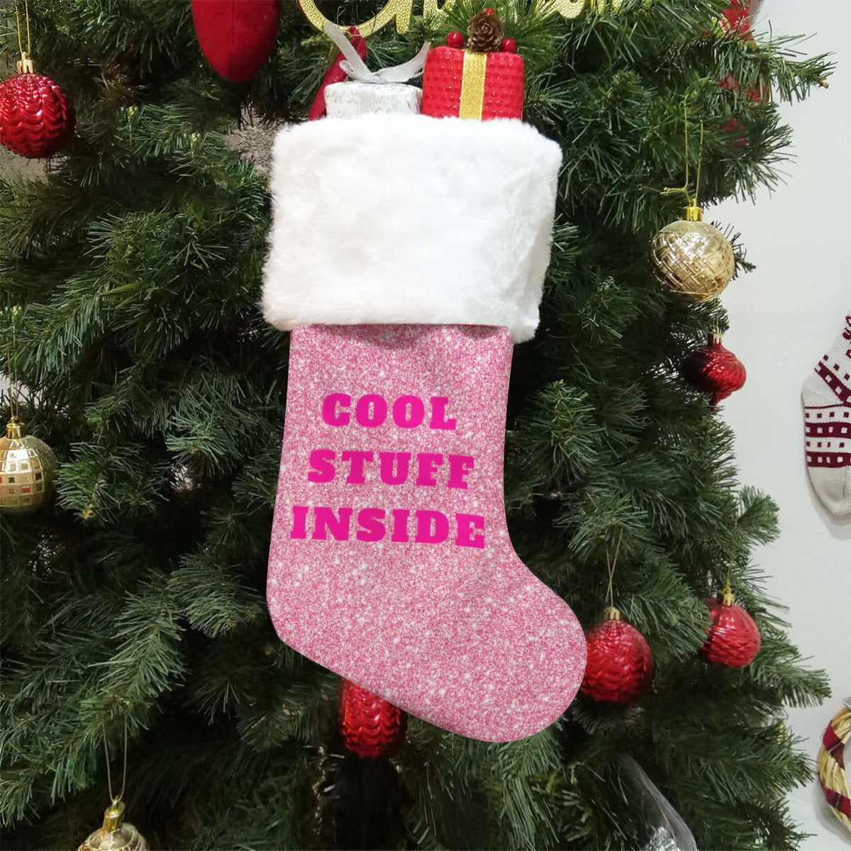 Pink Christmas stocking with 'Cool Stuff Inside' text hanging on a decorated tree.