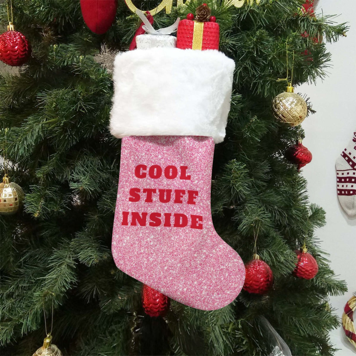 Pink Christmas stocking with 'Cool Stuff Inside' text hanging on a decorated tree.