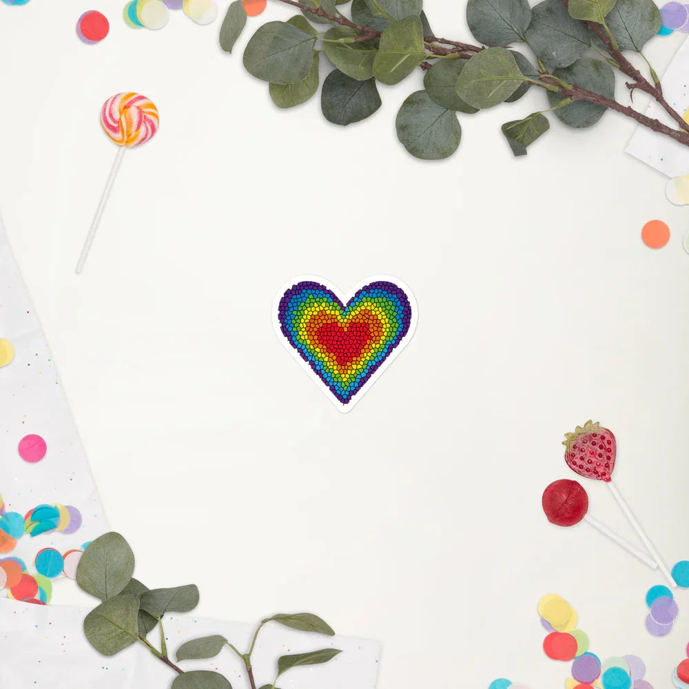 Colorful rainbow mosaic heart sticker on white background with lollipops, confetti, and eucalyptus leaves